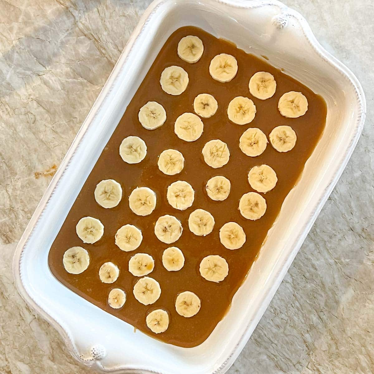 Process shot showing caramel sauce and bananas in bottom of casserole dish
