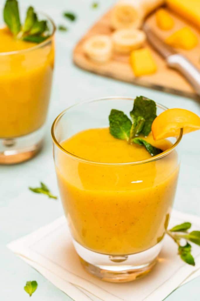 glass holding 2 serving of mango banana smoothie, with a 2nd glass behind with ingredients