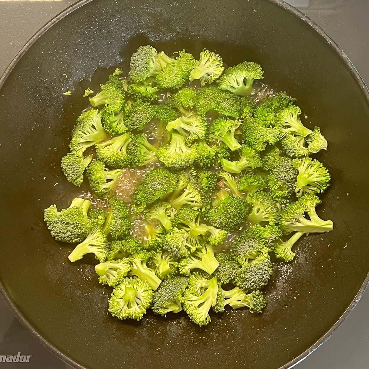 Steamed broccoli in a heated pan to make beef and broccoli stir-fry.