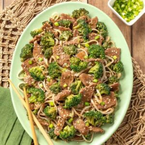 Easy beef and broccoli stir fry with rice noodles on a large platter with wooden chop sticks.