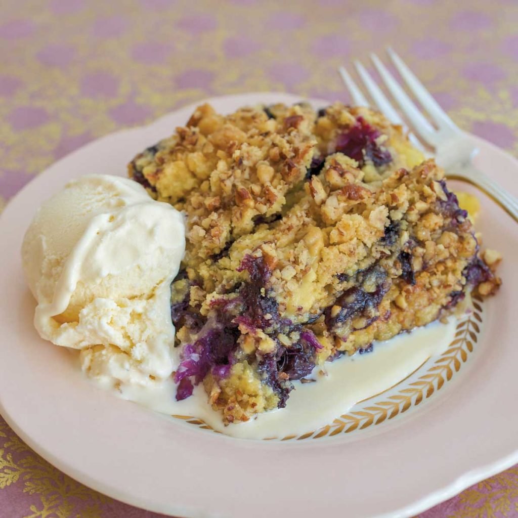 white plate holding a slice of Berry Cobbler, with a scoop if vanilla ice cream