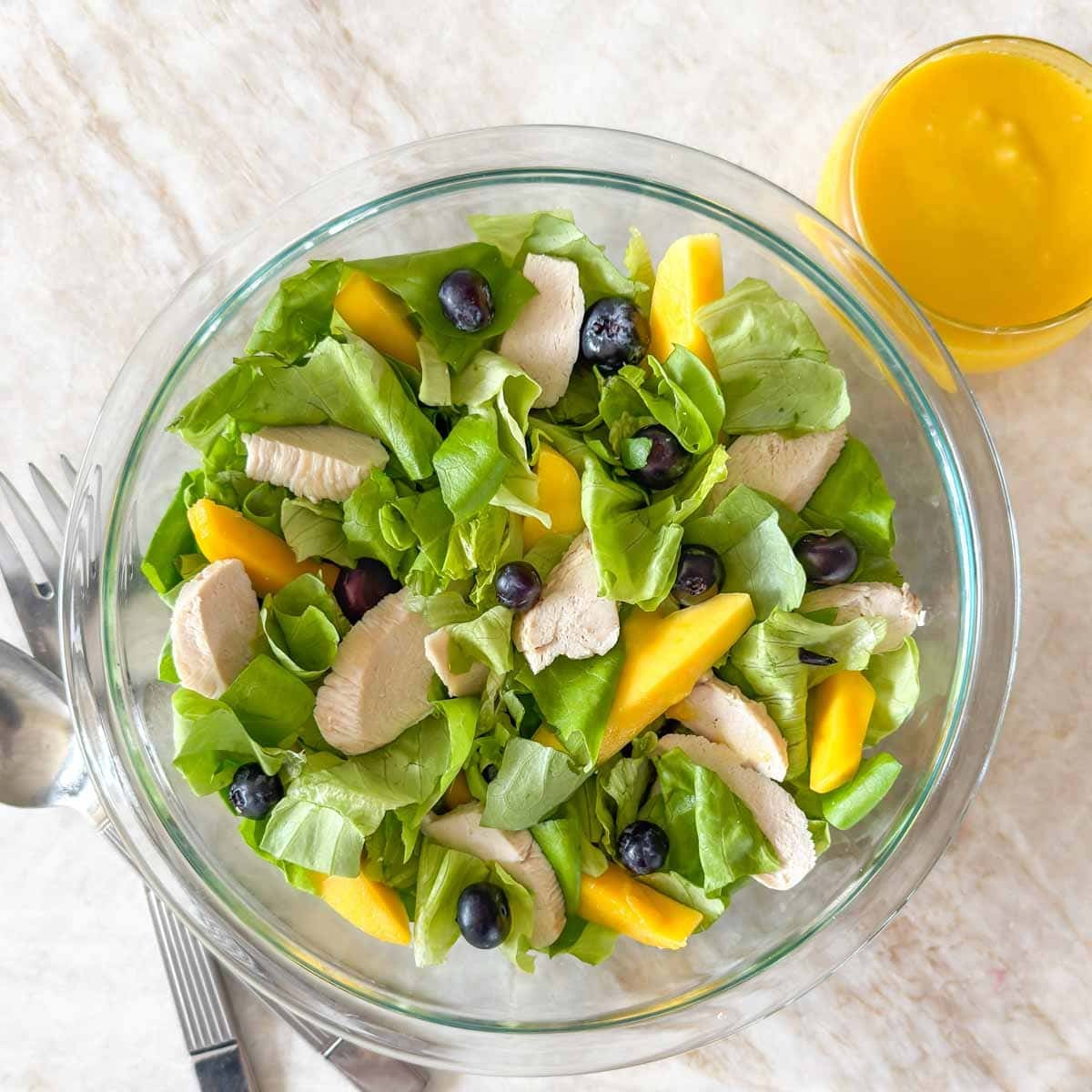 Lettuce, chicken, blueberries, and sliced mango loosely tossed in a bowl, ready to add dressing.