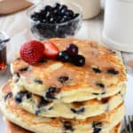 Stack of 4 golden brown blueberry buttermilk pancakes, topped with a few berries.