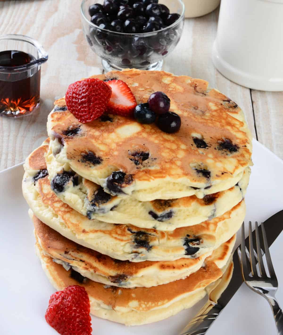 stack of blueberry pancakes with more berries and syrup on the side