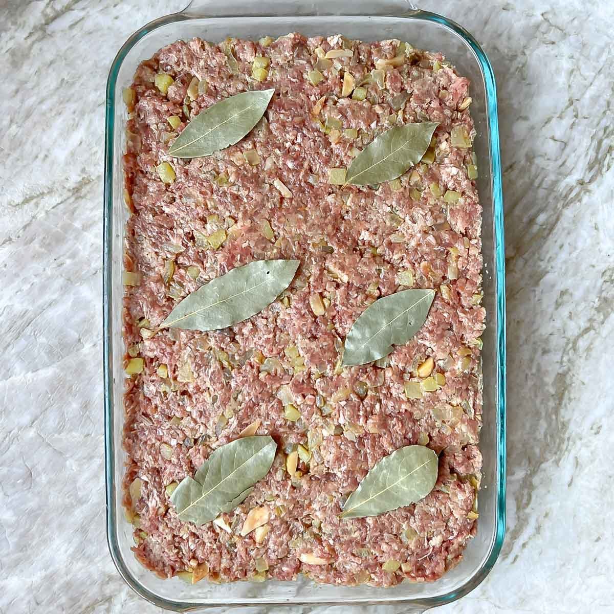Bobotie meat mixture packed into baking dish and topped with 6 large bay leaves