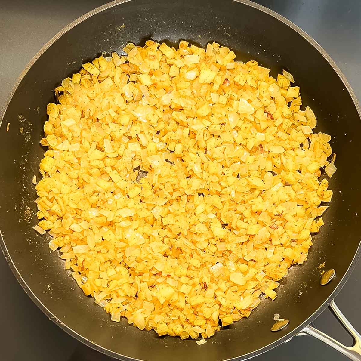 Chopped onion and apple with curry powder cooking in a large skillet
