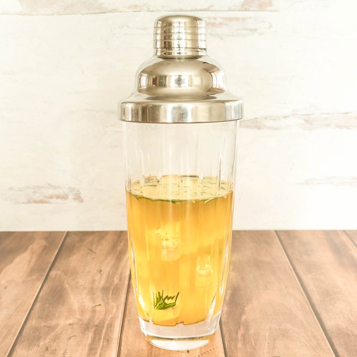 Side view of glass cocktail shaker with all lemon whiskey cocktail ingredients after shaking with ice.