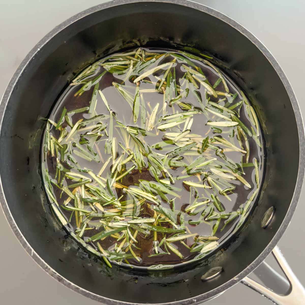 Honey simple syrup with rosemary leaves heating in a saucepan.