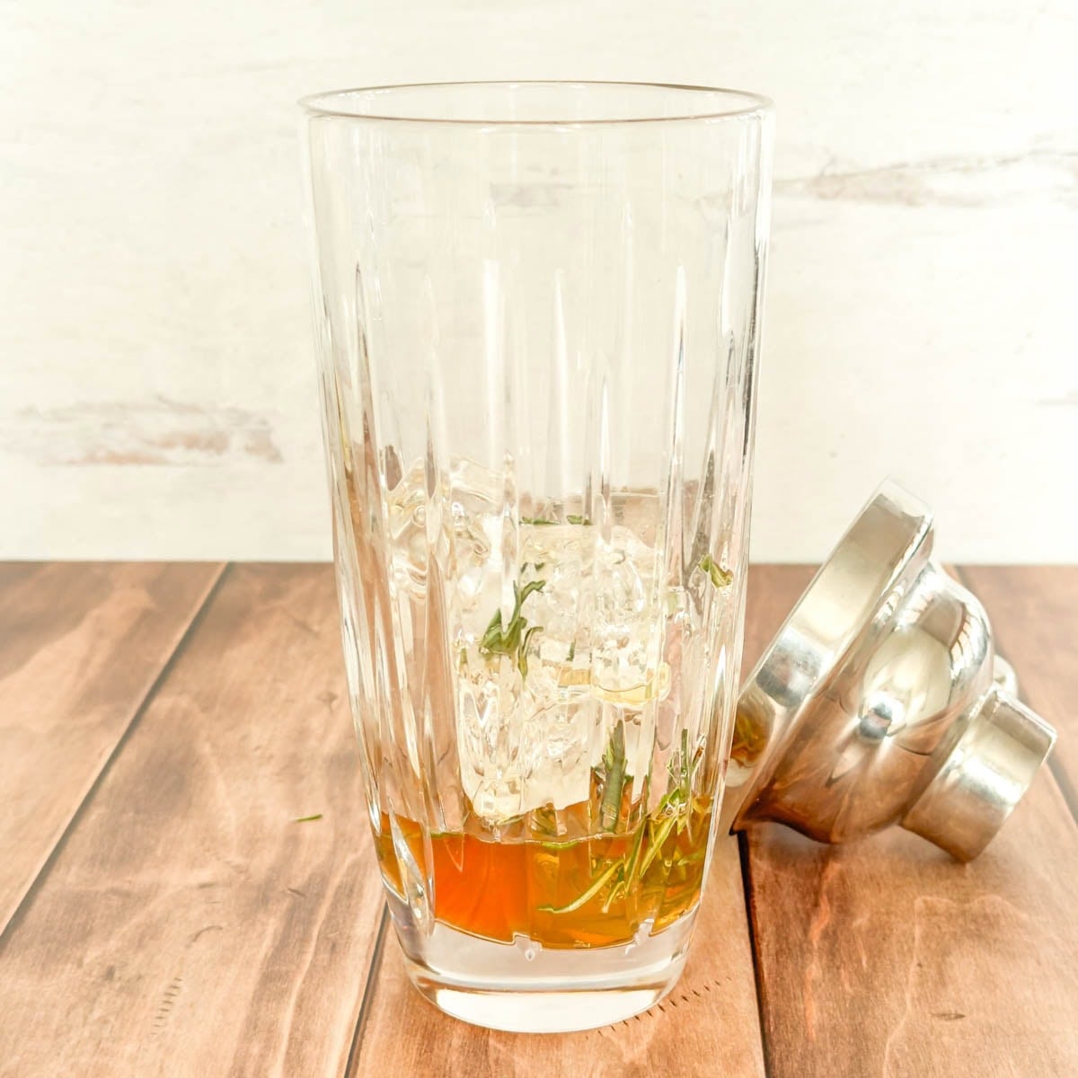Crystal cocktail shaker holding ice and rosemary simple syrup.
