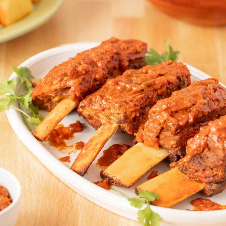 White platter holding 4 Spicy Beef Ribs with cornbread and salad in the back