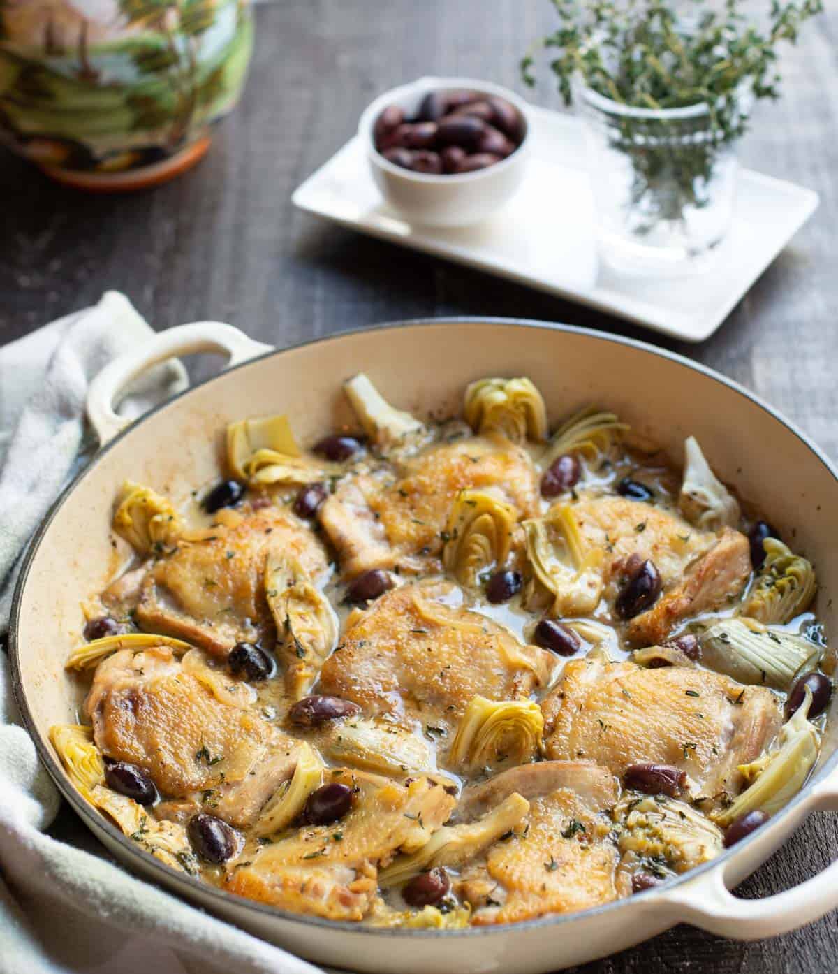 braised chicken thighs with olives and artichoke hearts in a shallow Dutch oven