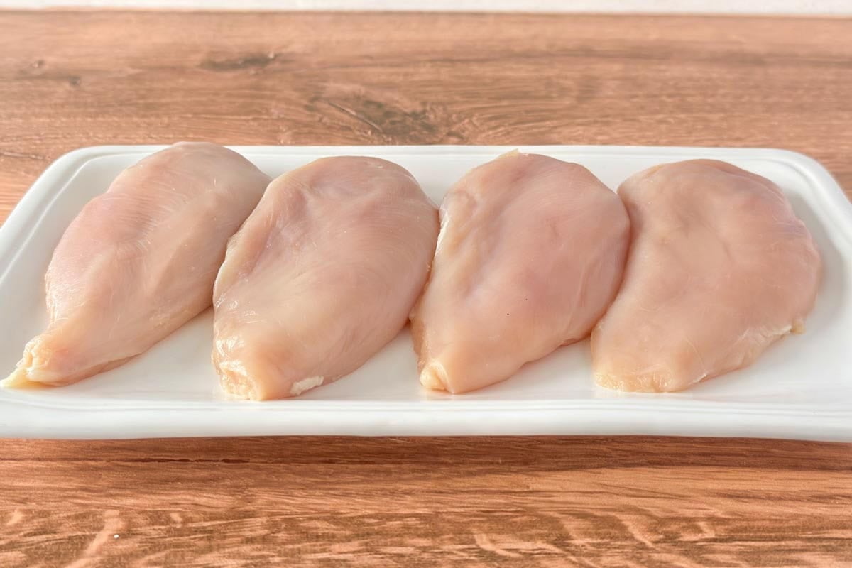 white platter holding 4 raw boneless, skinless chicken breasts.