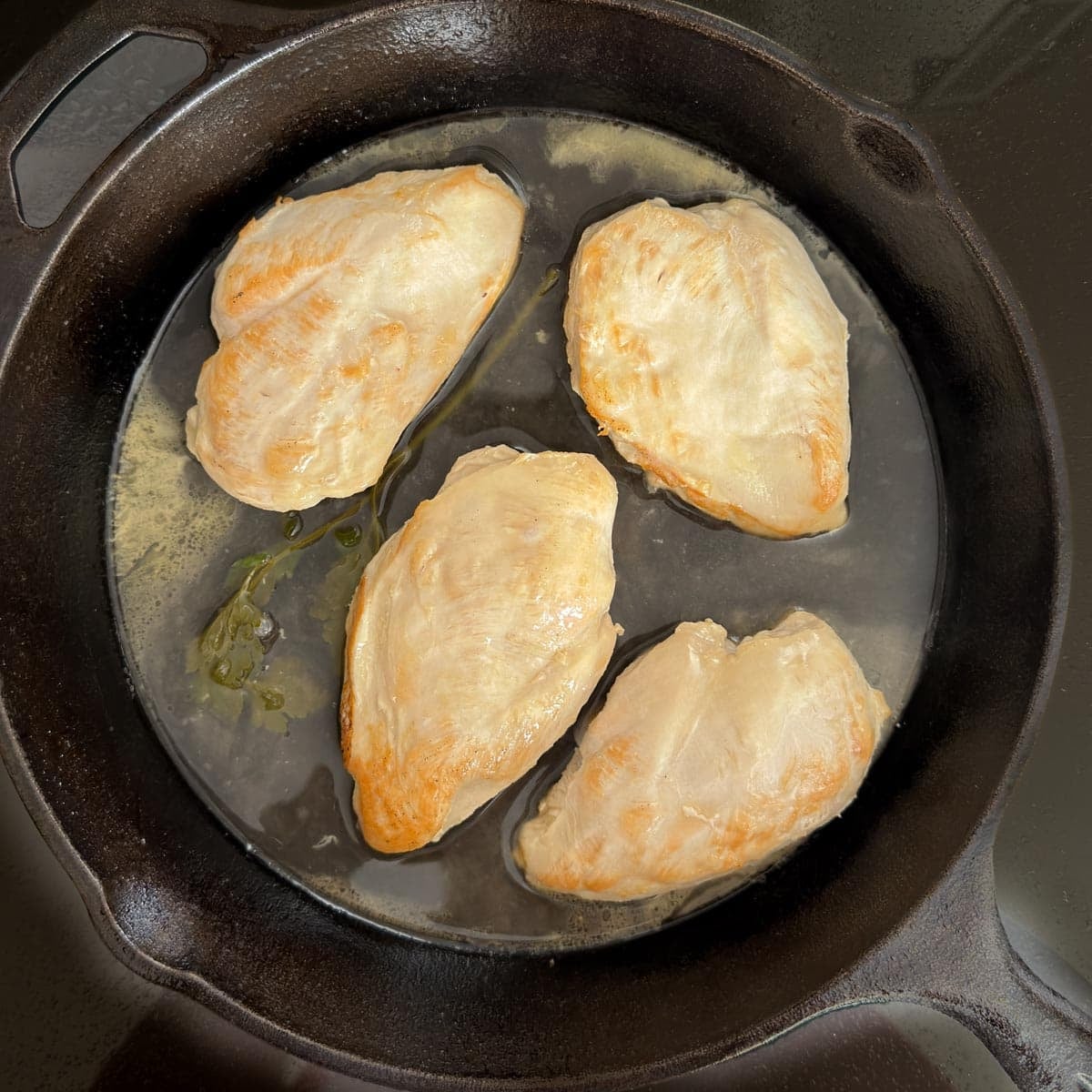 Braised chicken breasts resting in liquid inside cast iron skillet.