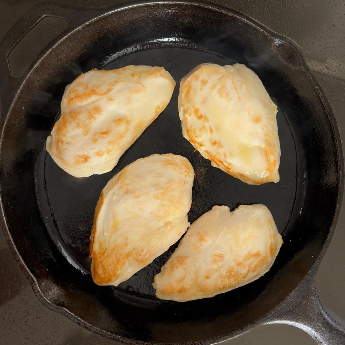 Cast iron skillet holding 4 boneless, skinless chicken breasts that have been lightly browned.