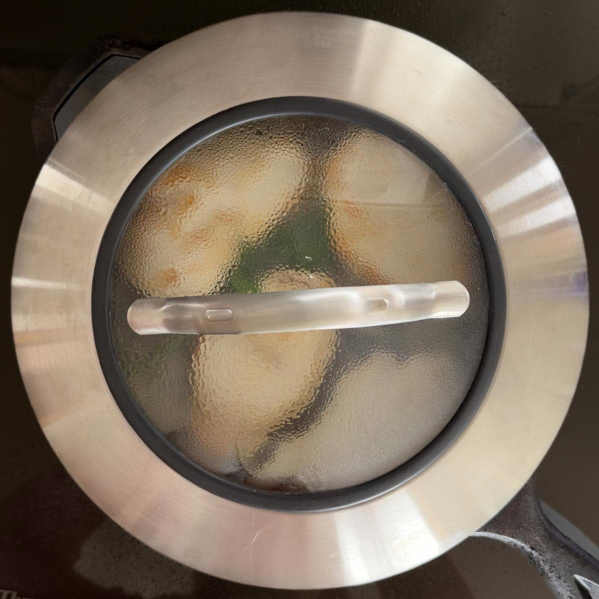 Covered cast iron skillet with chicken breasts braising inside.