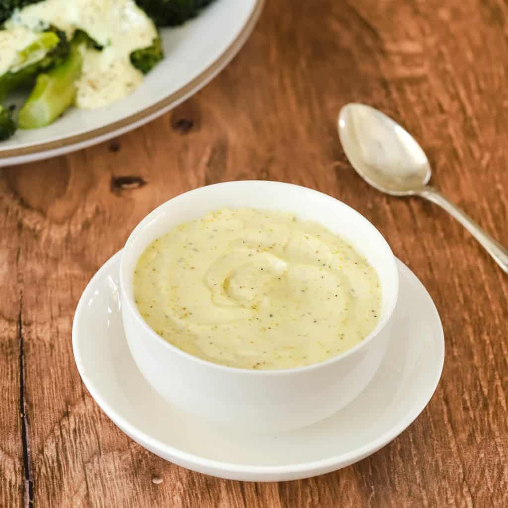 white bowl holding curry mayo sauce with a spoon on the side and broccoli in the background