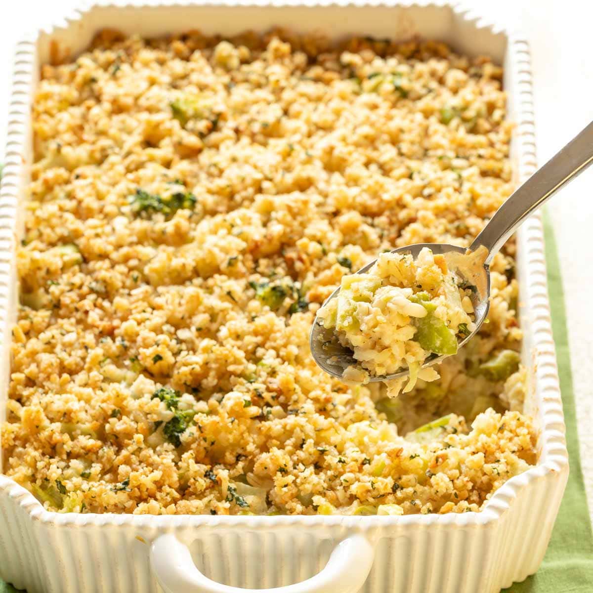 Spoon holding a scoop of Cheesy Broccoli Rice Casserole, hovering over the rest of the casserole