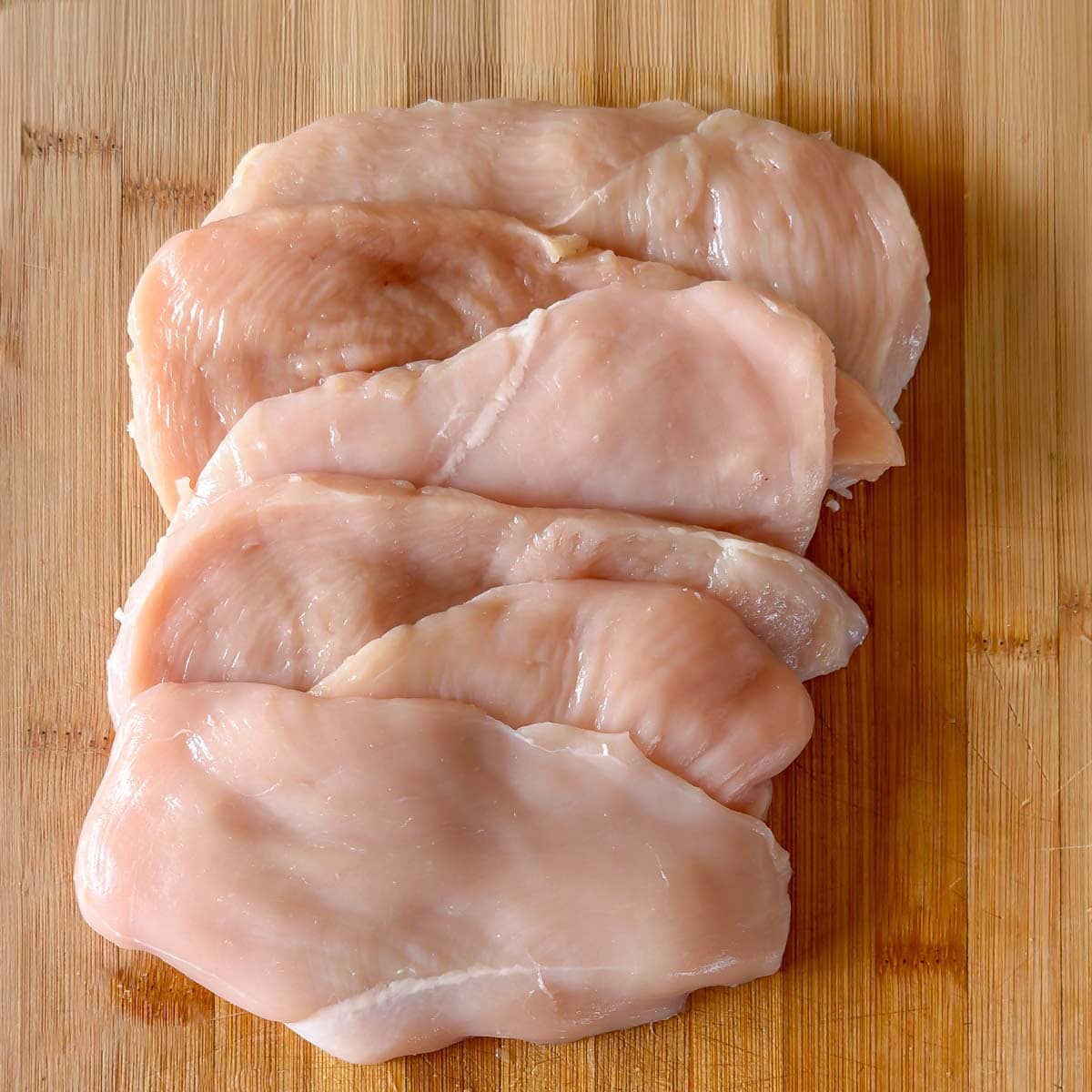 Raw butterflied chicken breasts ready for breadaing in chicken parmesan.