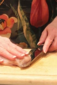Step one of butterflying a chicken breast - slicing from the side with hand on top