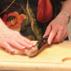 Step one of butterflying a chicken breast - slicing from the side with hand on top