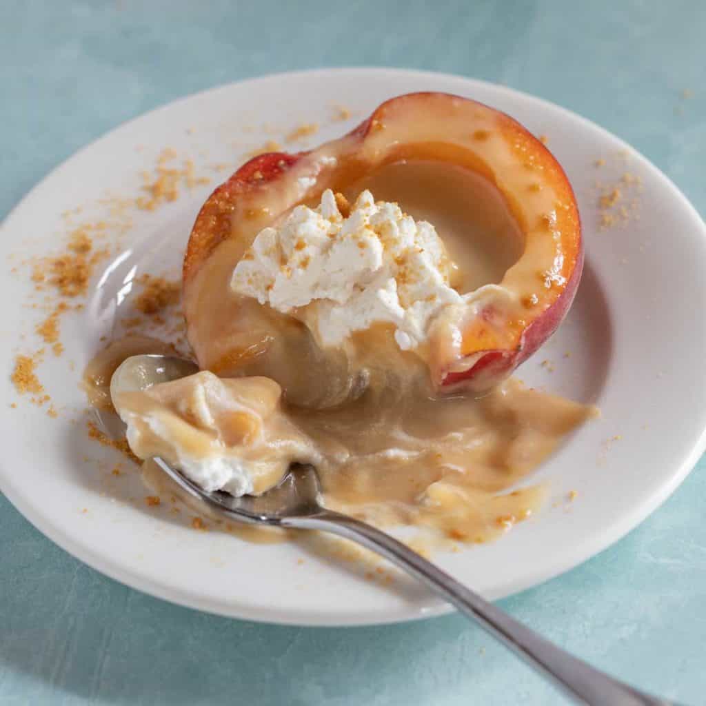 white plate with a Butterscotch Pudding Filled Peach half, with the filling oozing out on the plate