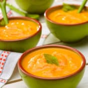Three bowls of Creamy Carrot Ginger Soup with celery leaf garnish