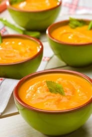 Three bowls of Creamy Carrot Ginger Soup with celery leaf garnish