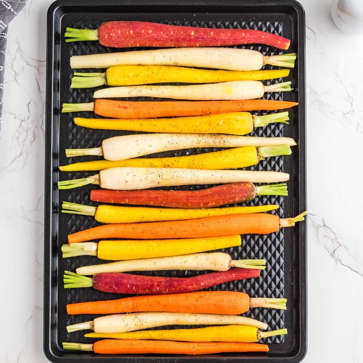 Baby carrots lined up on a roasting pan.