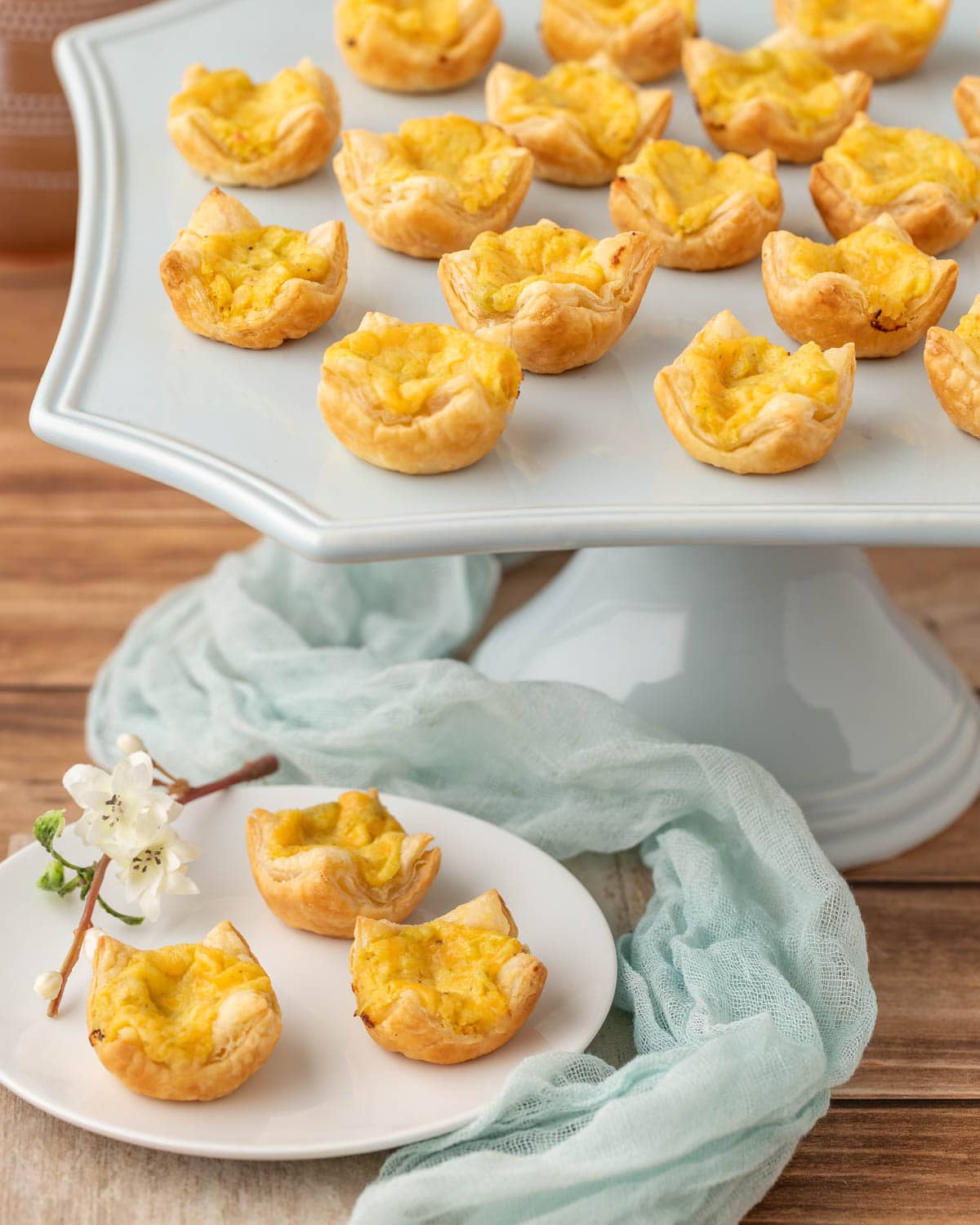 pale blue stand holding a portion of Mini Cheese Tarts with 3 on a plate in front