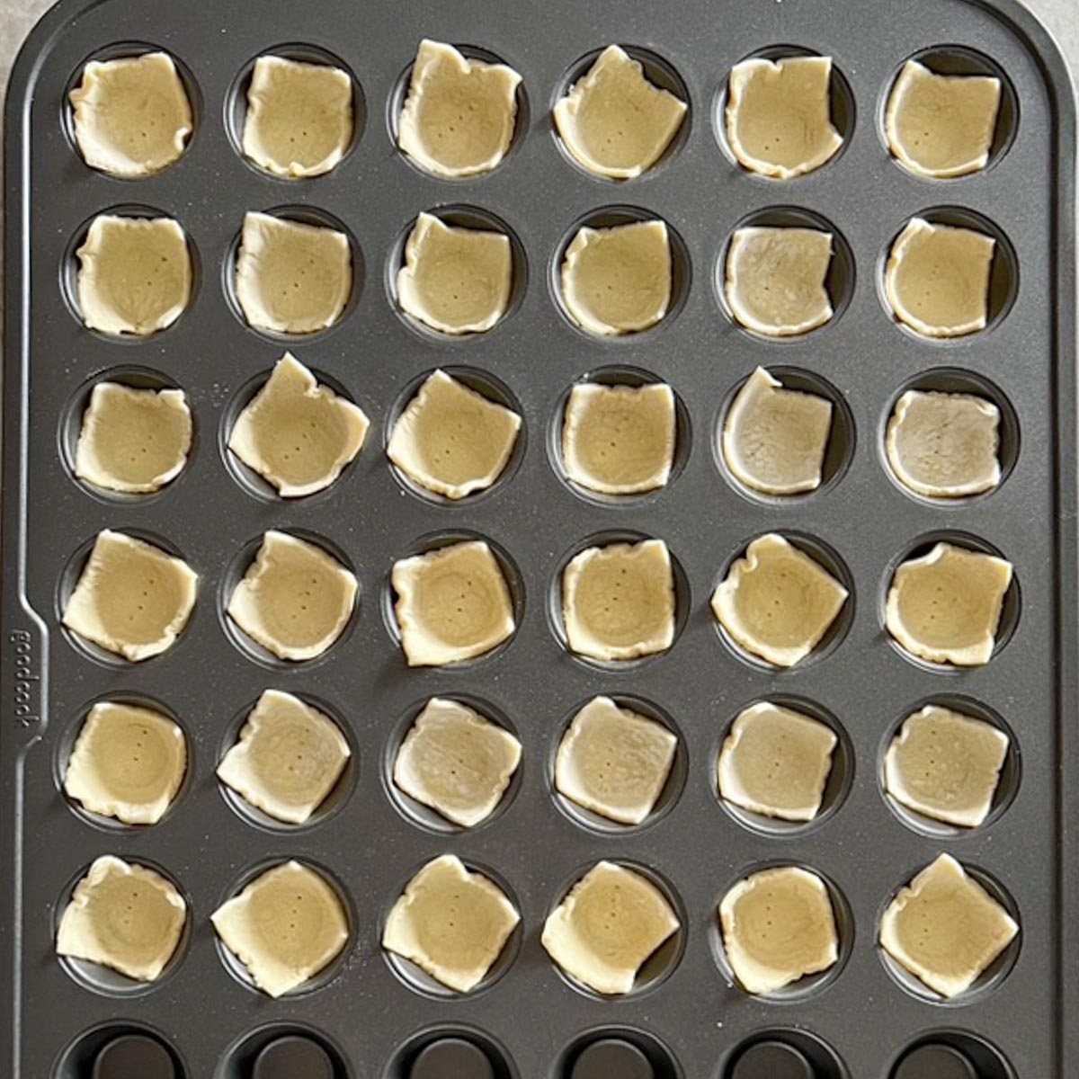 Mini muffin tin holding puff pastry squares, unfilled