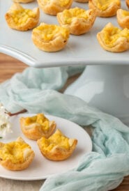 pale blue stand holding a portion of Mini Cheese Tarts with 3 on a plate in front