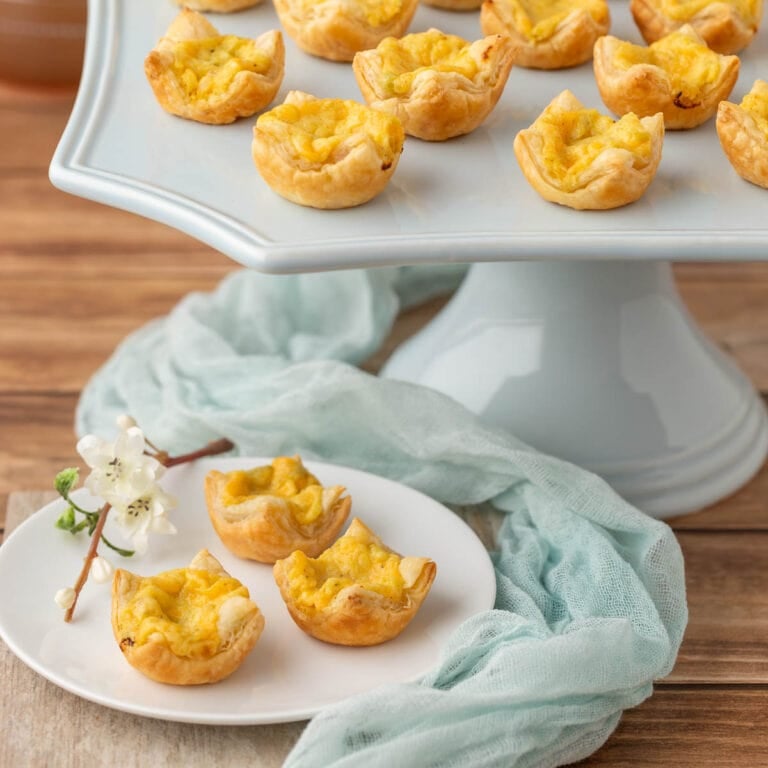 pale blue stand holding a portion of Mini Cheese Tarts with 3 on a plate in front