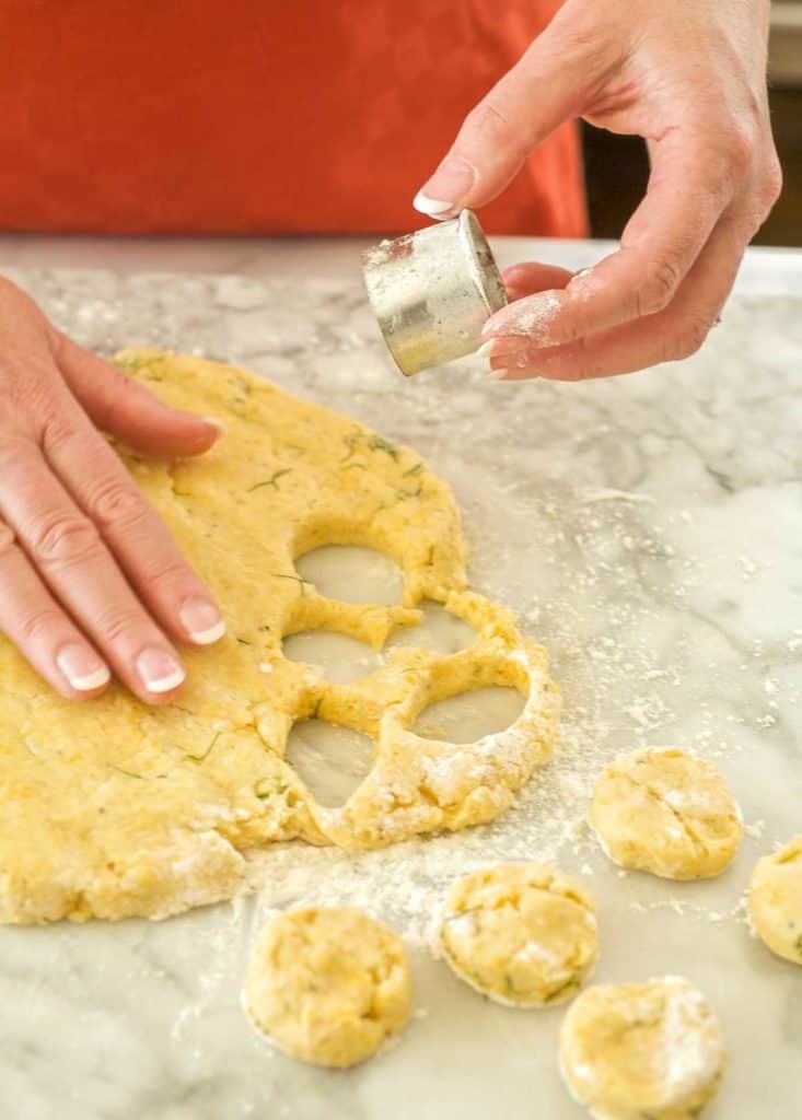 Showing how to cut out Mini Cheddar Dill Scones. Dough is on marble slab and partially cut out.