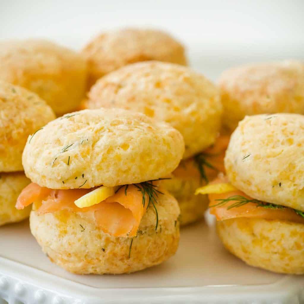 white plate holding several Mini Cheddar Dill Scones filled with smoked salmon