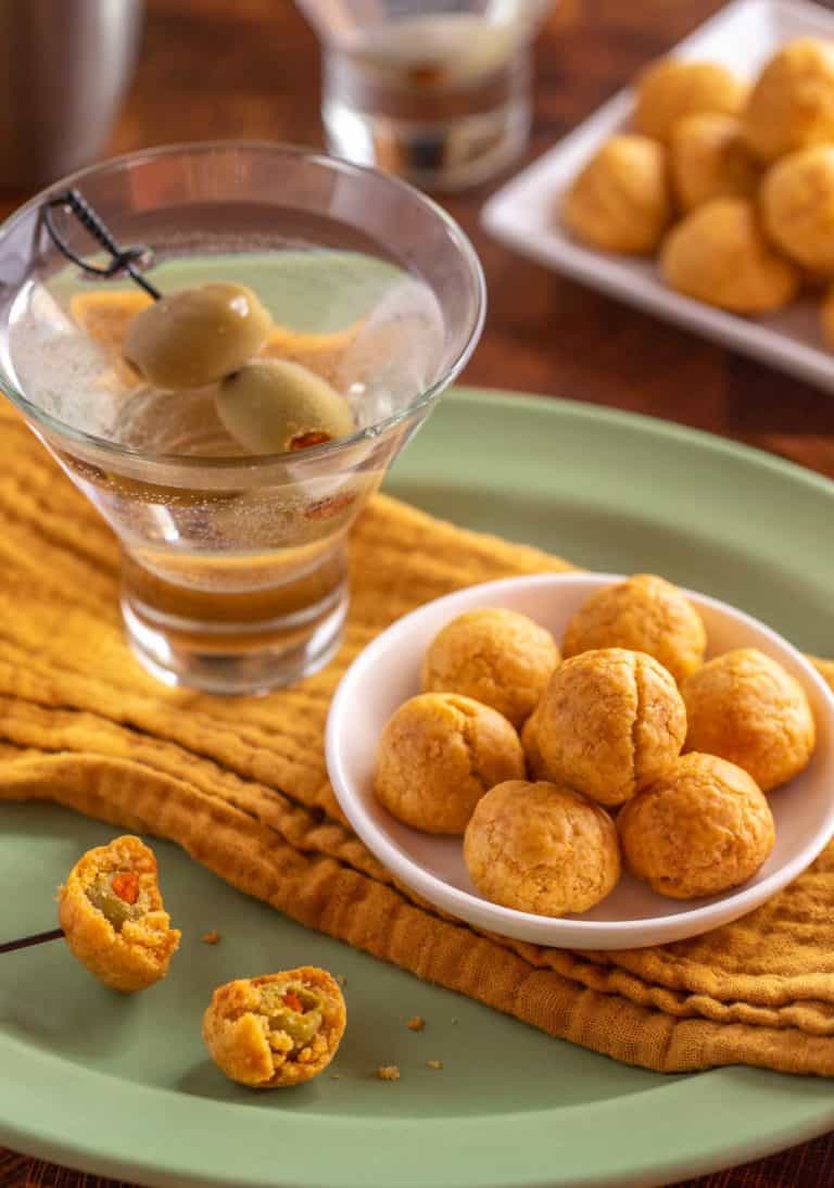 small white plate holding a few Olive Cheese Balls, sitting next to a martini