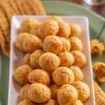 large white platter holding many Olive Cheese Balls, sitting on top of an orange napkin and a green platter