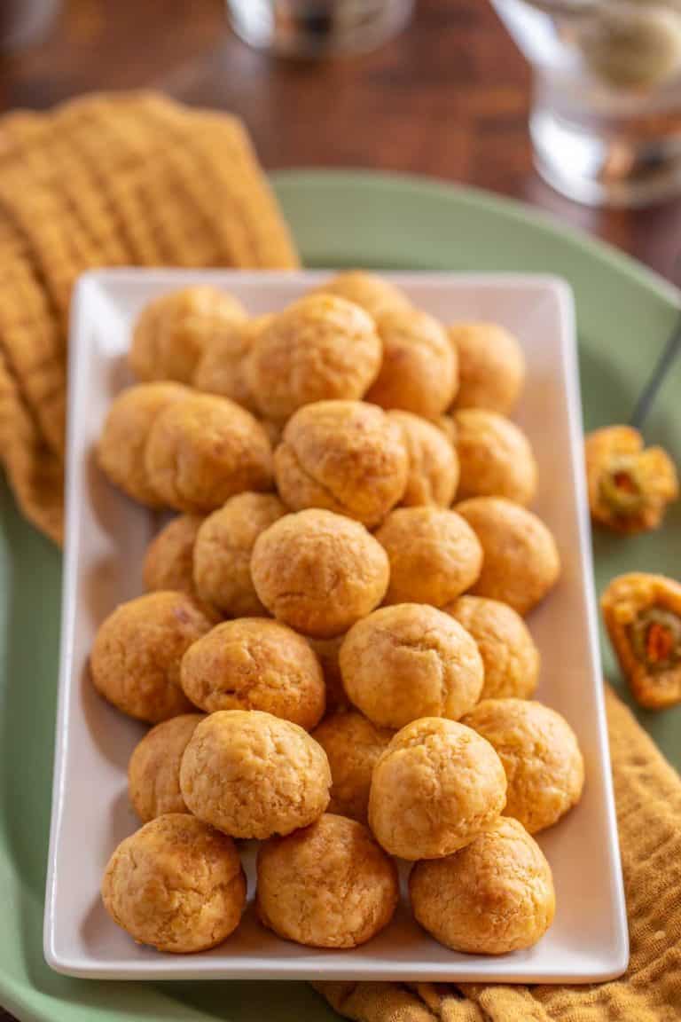 large white platter holding many Olive Cheese Balls, sitting on top of an orange napkin and a green platter