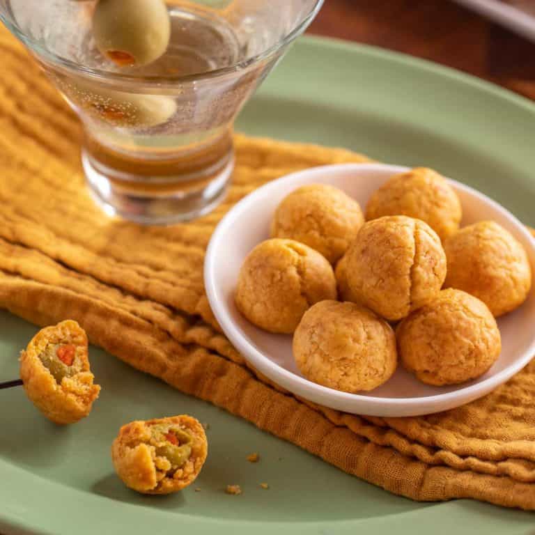 small white plate holding a few Olive Cheese Balls, sitting next to a martini