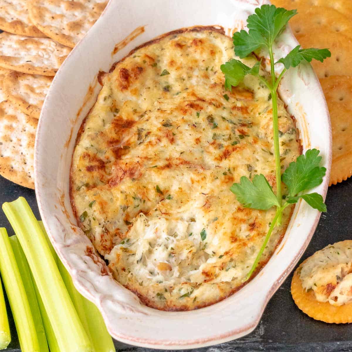 close up overhead view of ot crap dip with a portion removed, showing the inside with crackers and celery sticks alongside.