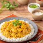A portion of Chicken Curry with Coconut Milk atop basmati rice with toppings on the side