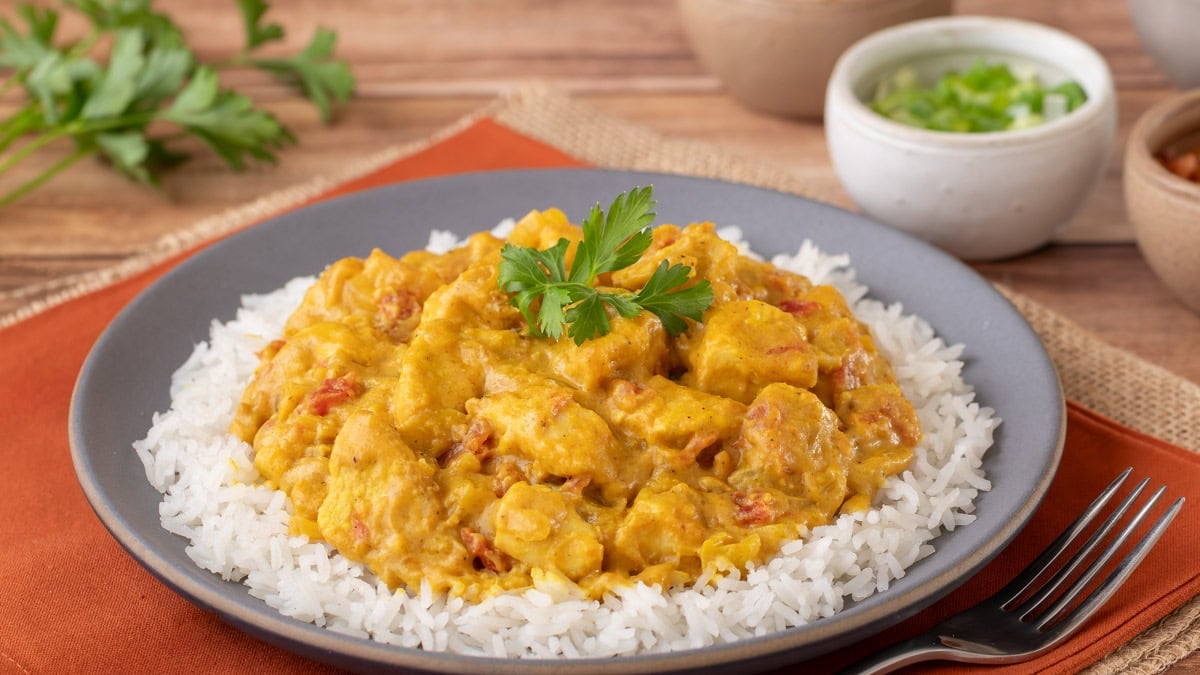close up view of A portion of Chicken Curry with Coconut Milk atop basmati rice with a few toppings on the side