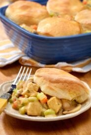 plate holding one portion of chicken pot pie with biscuits, with baking dish holding the rest in the background