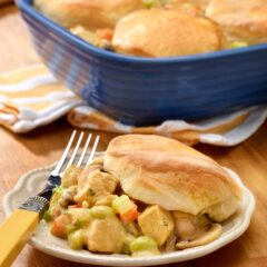 plate holding one portion of chicken pot pie with biscuits, with baking dish holding the rest in the background