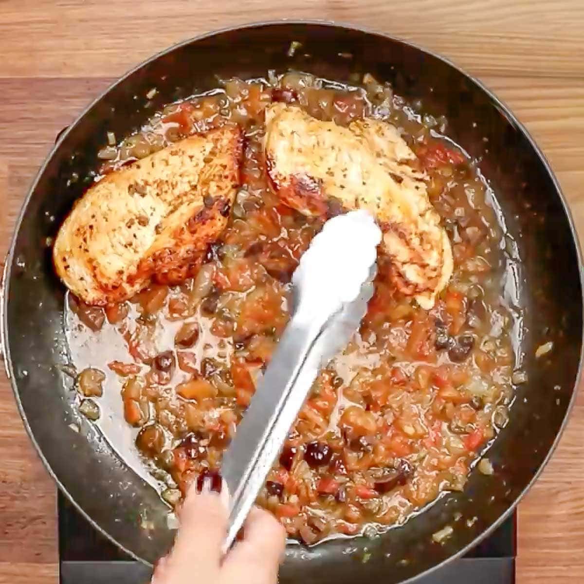 Adding the chicken back to the skillet of olives and tomatoes. 