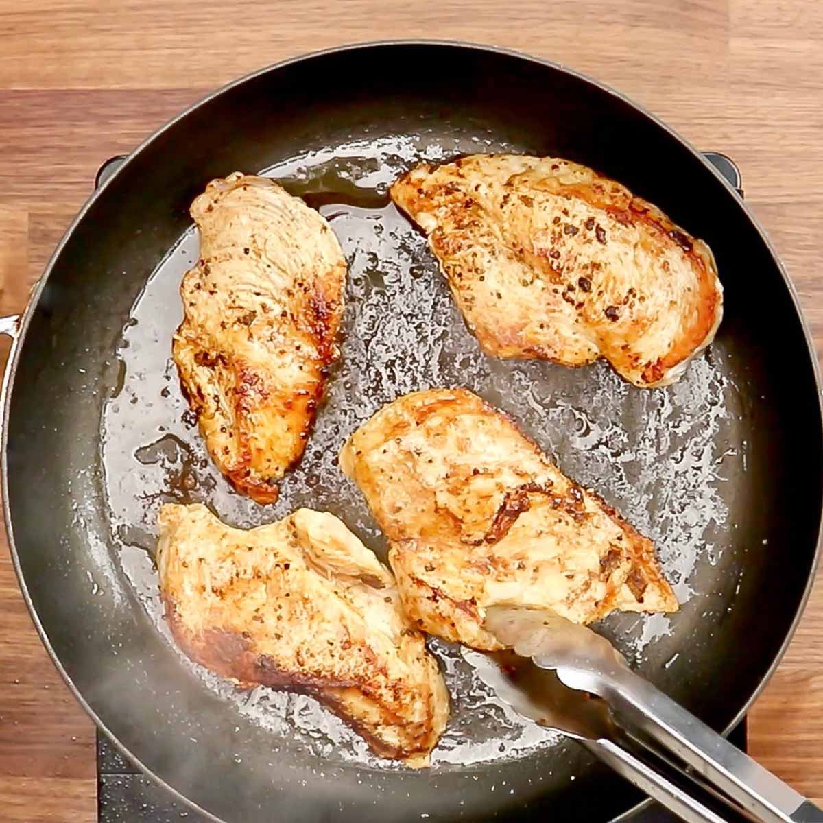 Chicken breasts cooking in a skillet. 