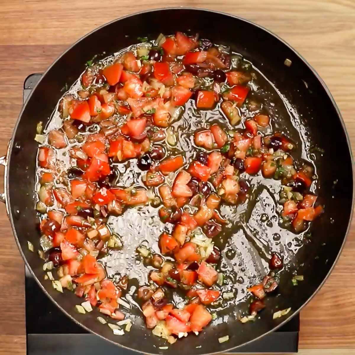 Tomatoes and onion added to a skillet with olive oil. 