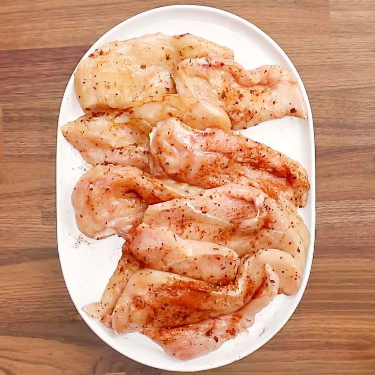 Seasoned chicken breasts on a platter. 