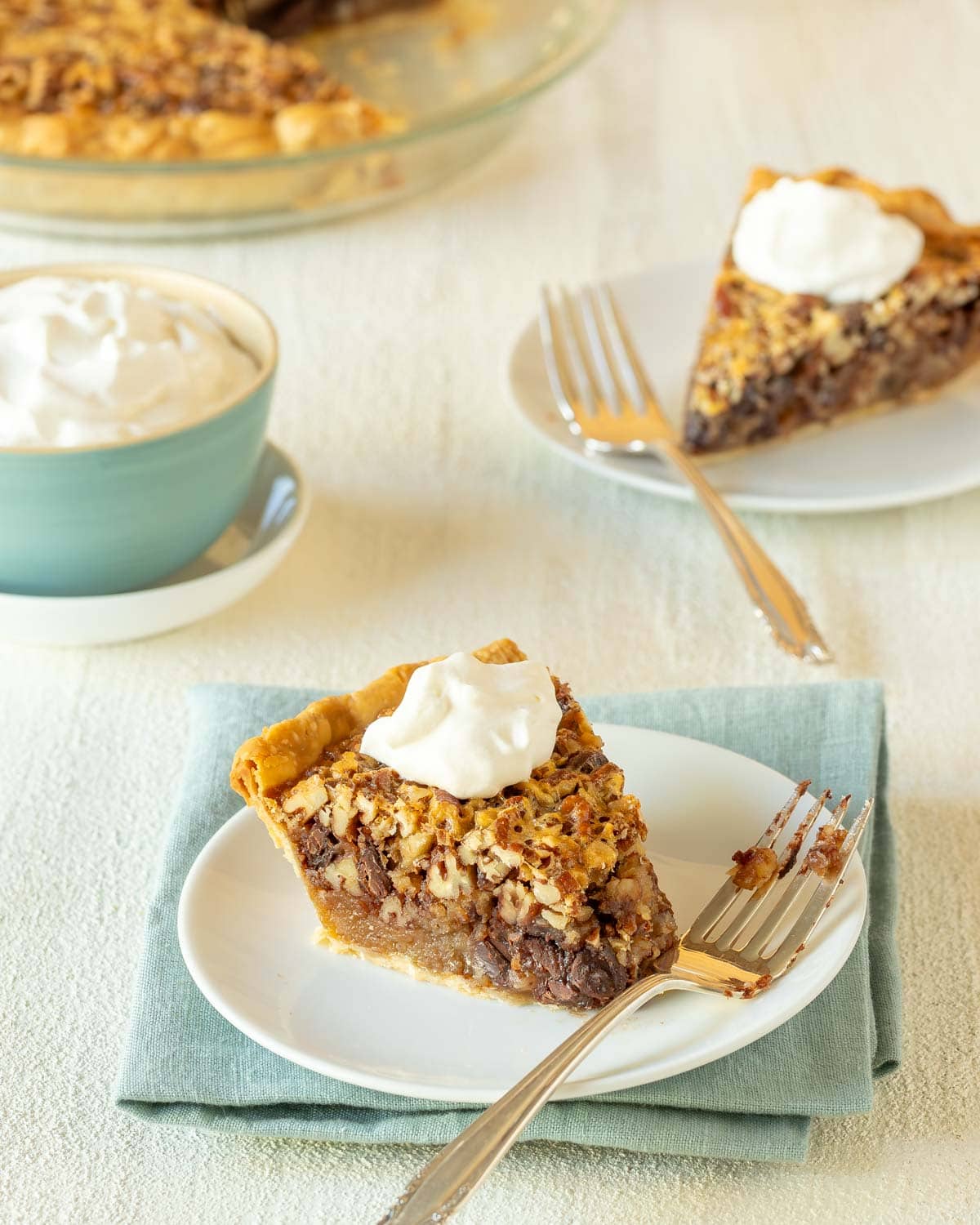 Two slices of Chocolate Pecan Pie topped with whipped cream, with a bowl of whipped cream alongside