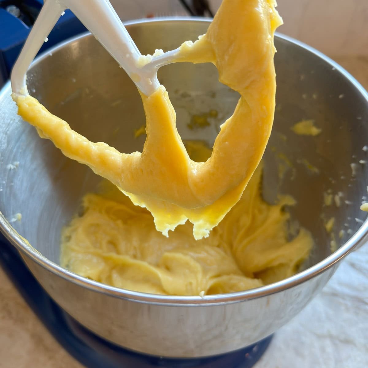 choux pastry in bowl of stand mixer, with paddle lifted up showing the dough breaking off in a V shape.