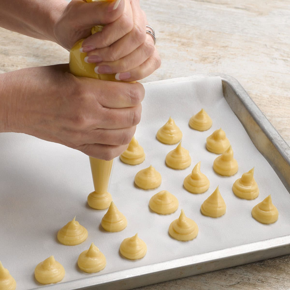 Piping choux pastry into mounds on a parchment lined baking sheet